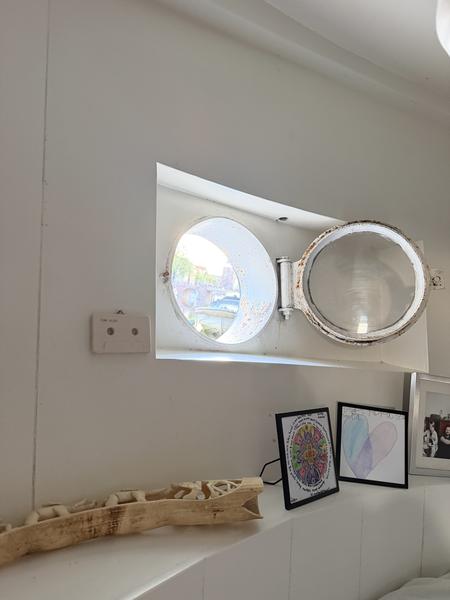 This photo captures a bright, cozy interior space, likely a houseboat, featuring a distinctive open porthole window